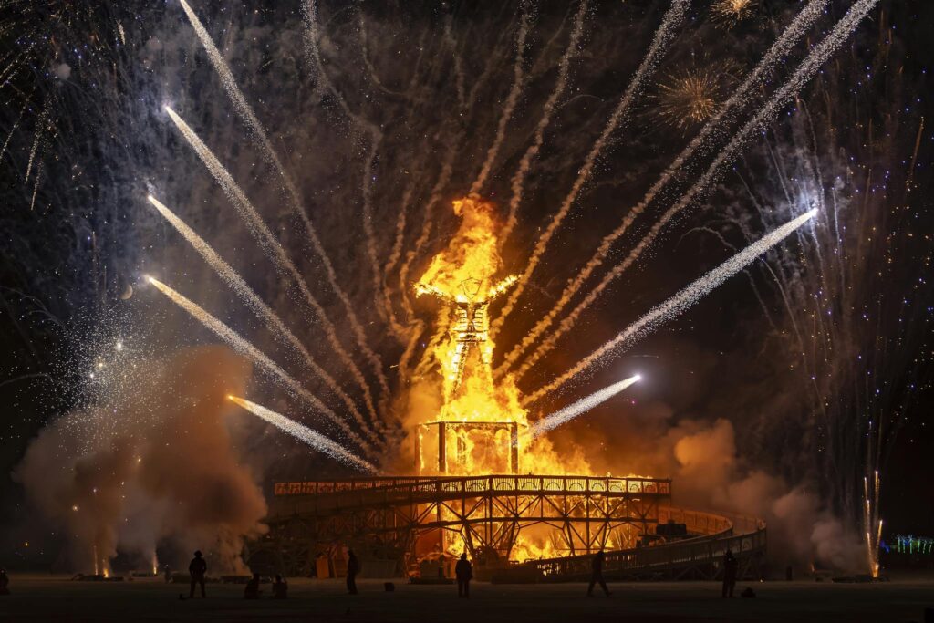 The iconic Burning Man effigy ablaze with surrounding fireworks at night.